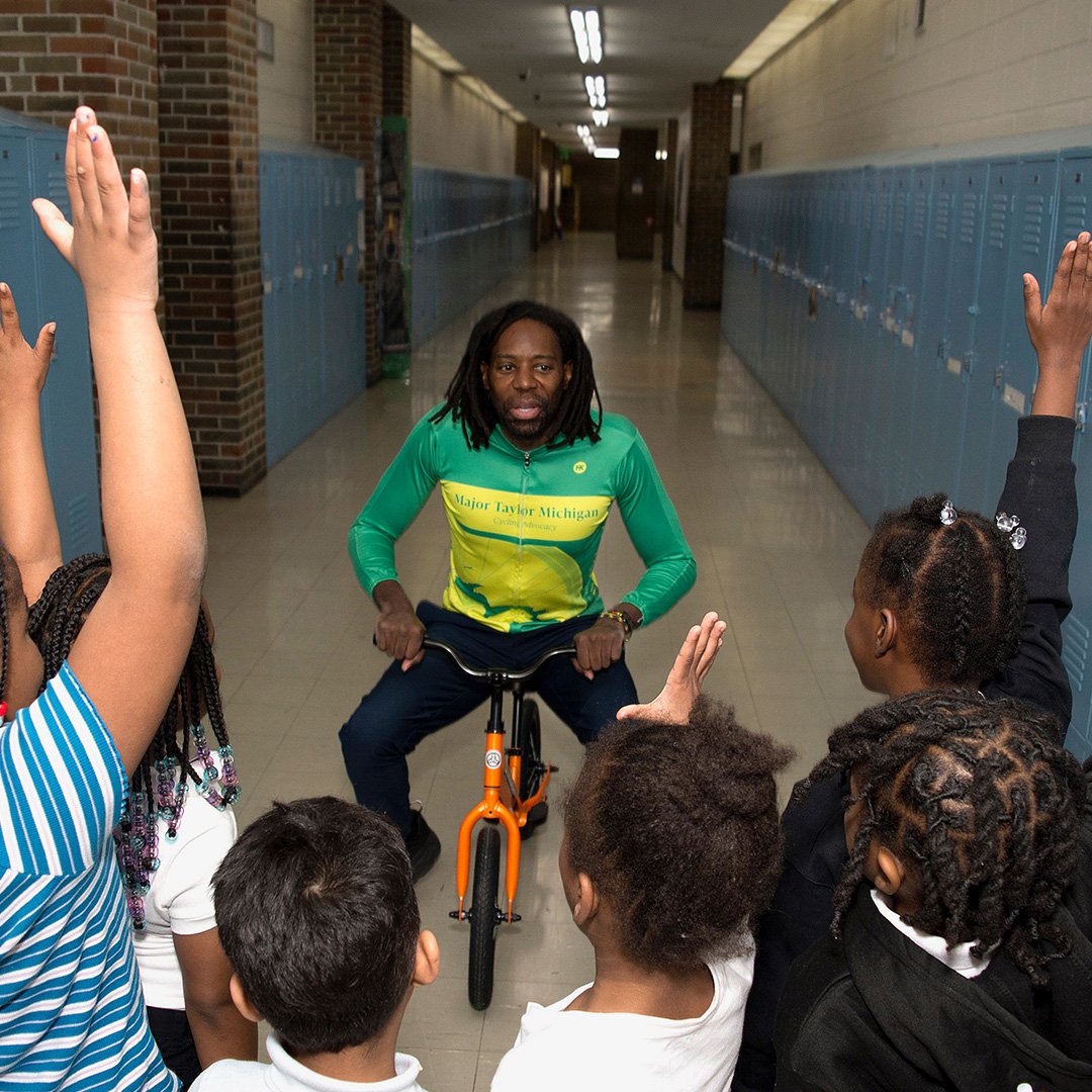 Children watching a cyclist in hallway.